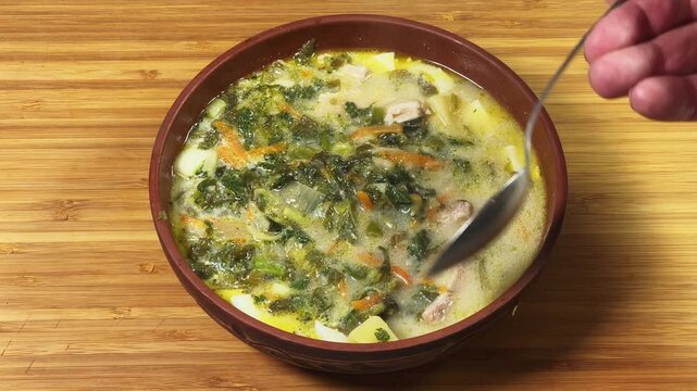 Stirring with spoon of sorrel soup in bowl on wooden surface