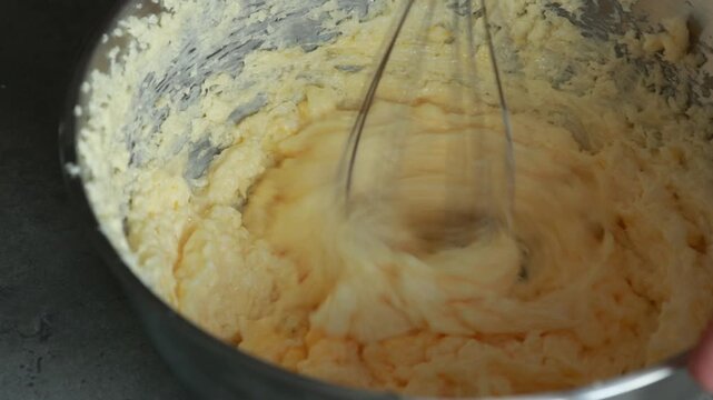 Close-up of a child's hands adding an egg into a butter and sugar mixture while using a hand mixer