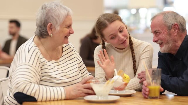 Grandparents and teenage girl sitting at table in cafe. Light snack or coffee break at restaurant, family getaway or pastime. Family time, Sunday lunch at chain cafe