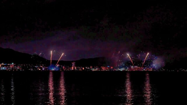 Spectacular fireworks display over the city skyline and the lake reflecting in the water at night for the New Year or Fourth of July celebration.
