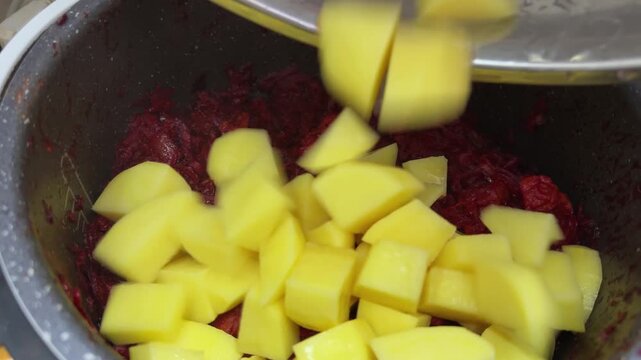 Adding potatoes to stewed vegetables with meat for borscht cooking