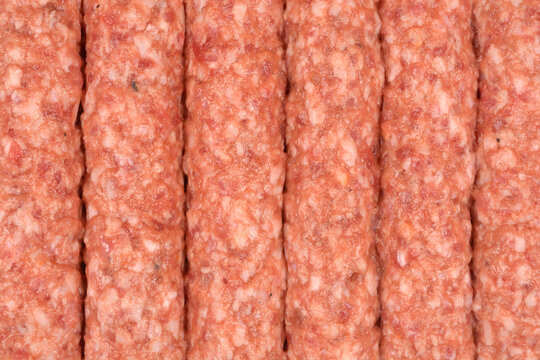 A close up shot of raw cevapcici sausages made from seasoned minced meat arranged in rows with visible fat and protein texture