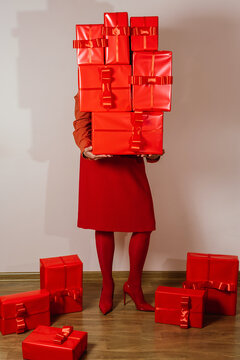 Faceless woman in red outfit holding stack of red gift boxes indoors