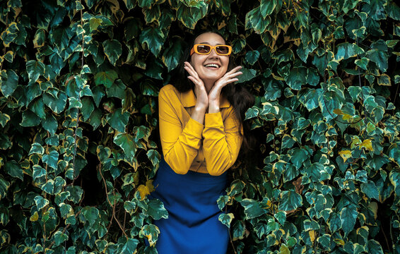 Smiling nature lover in yellow shirt and sunglasses by an ivy wall