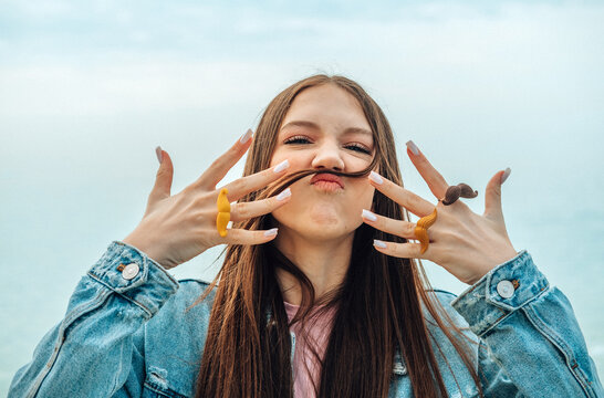 Playful teenage girl making a fake mustache with her hair outdoors