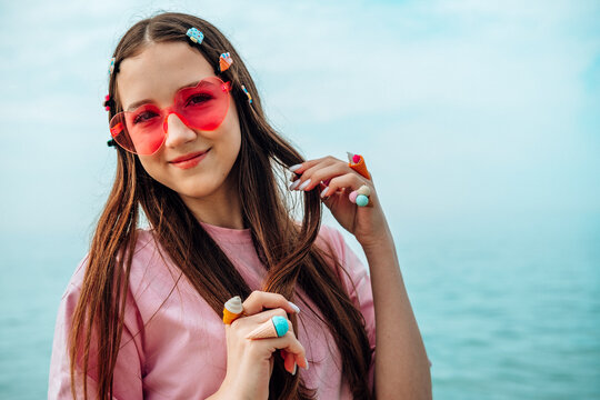 Smiling teenage girl in pink sunglasses playing with hair by the sea