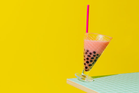 Strawberry bubble tea balancing on table edge against yellow backdrop