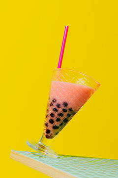 Tilted pink strawberry bubble tea glass on yellow background