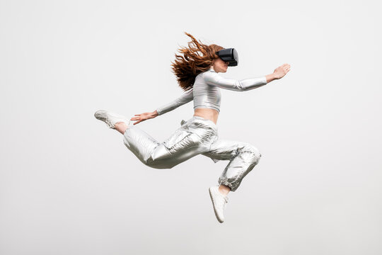 Futuristic red haired gamer jumping outdoors with VR headset