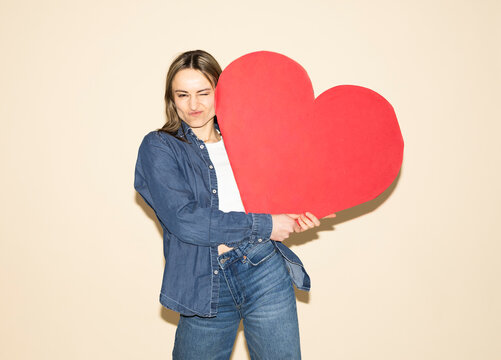 Model in jeans outfit holding a red paper heart and winking