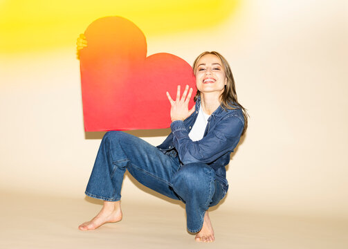 Smiling model in jeans outfit holding red paper heart