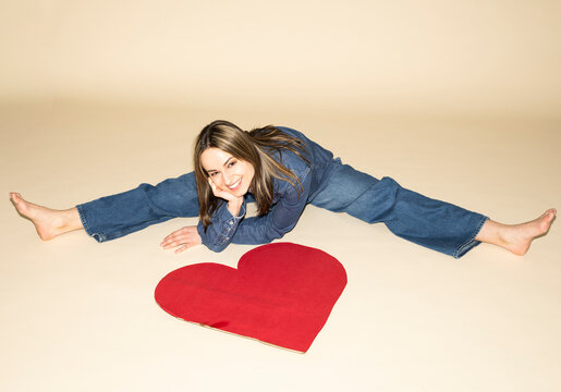 Smiling model in denim outfit sitting with a red paper heart