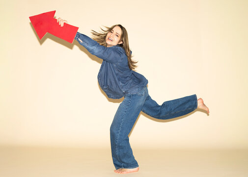 Woman jumping happily in denim holding a red paper arrow pointing forward
