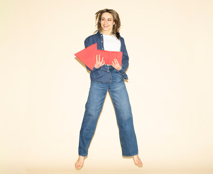 Woman jumping in denim outfit holding red paper arrow for direction