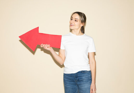 Smiling woman holding red paper arrow showing direction