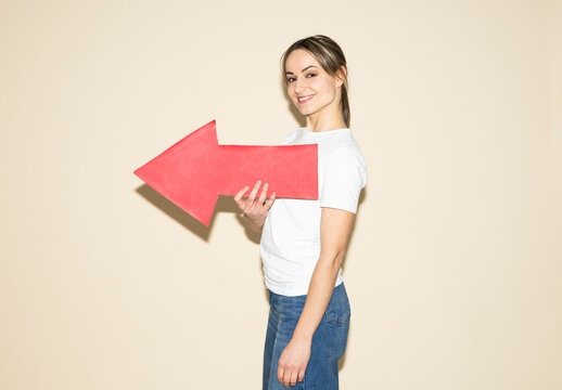 Smiling woman holding red paper arrow showing direction indoors