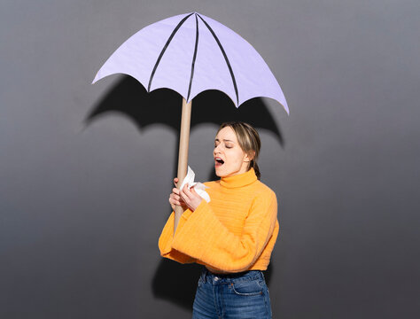 Woman sneezing into a tissue holding a purple paper umbrella