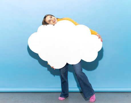 Woman holding a large blank paper cloud against a blue studio background