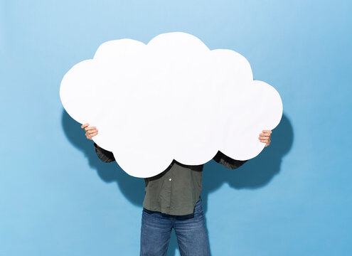 Anonymous person holding blank paper cloud over face indoors