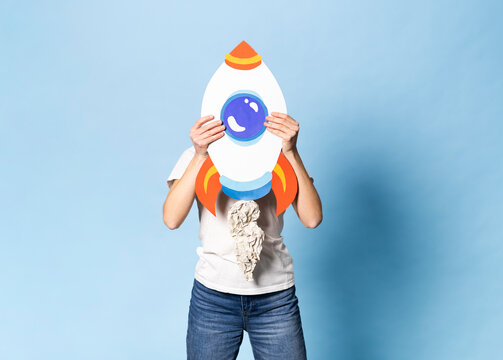 Woman holding a handmade paper rocket over face indoors for success