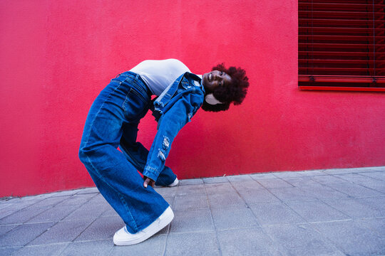 Flexible urban dancer with headphone leaning back on red wall