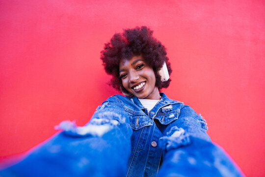 Smiling music fan with headphone taking selfie on red background