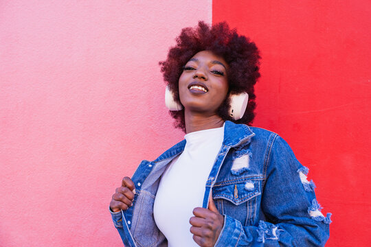 Smiling model in denim jacket listening to music by pink wall