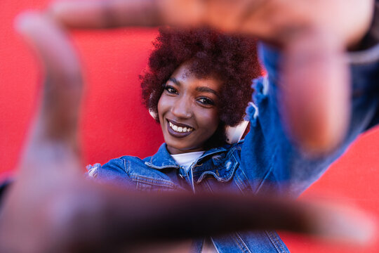 Smiling woman with afro making finger frame against red wall