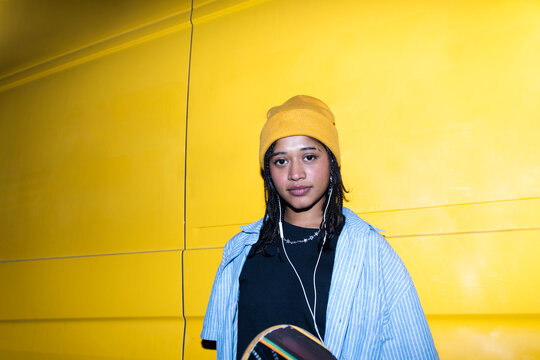 Portrait of skateboarder with headphone on yellow night background