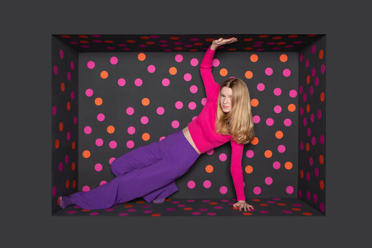 Blond teenager touching alcove against black background with colored dots