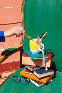 Hand reaching for pen on stacked colorful books and an armchair