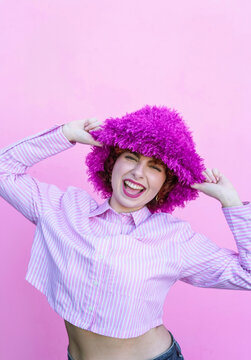 Redhead posing playfully in a purple hat on a pink background