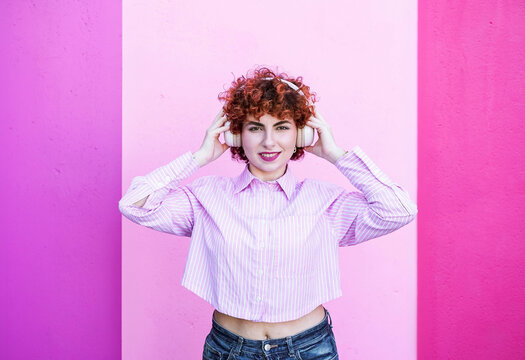Redhead holding headphone smiling on pink background