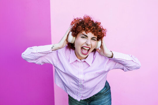 Redhead with headphones singing loudly on pink background