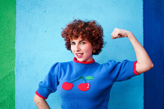 Strong redhead flexing bicep with attitude against colorful wall
