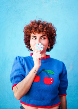 Portrait with curly red hair holding a flower and looking away