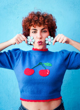 Redhead woman in blue sweater holding flower prop making funny face