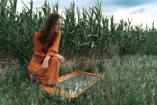 Woman looking in mirror crouching by corn crops in field