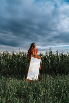 Woman with mirror in front of cloud at corn field