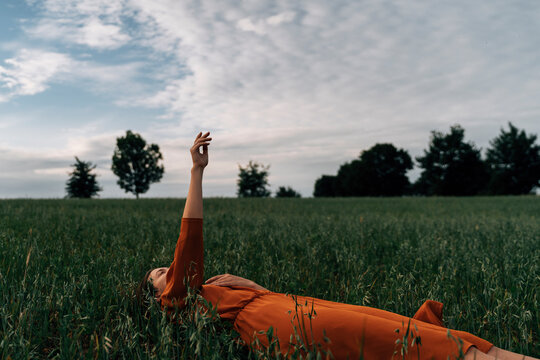 Woman gesturing with hand raised lying in field at sunset