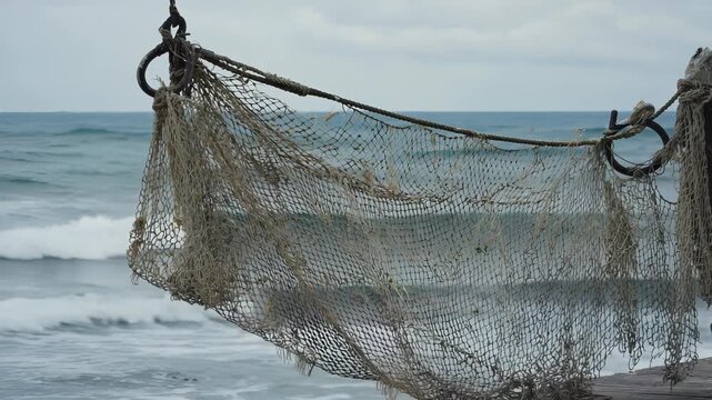 Weathered fishing net suspended over the ocean from a rustic pier, symbolizing coastal life, maritime traditions, and the endless cycle of the sea.