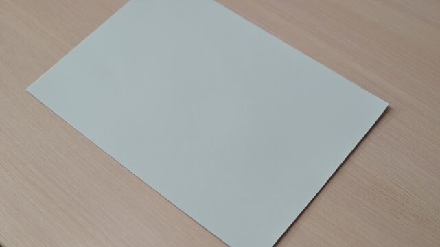 Hands perform a series of folds on white paper placed on a wooden table. This action demonstrates techniques suitable for crafting, design projects, or educational materials