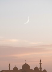 Obraz premium Soft pink twilight sky background with crescent moon and mosque silhouettes at sunset for Ramadan Kareem, Eid Mubarak greeting and Islamic vertical banner template