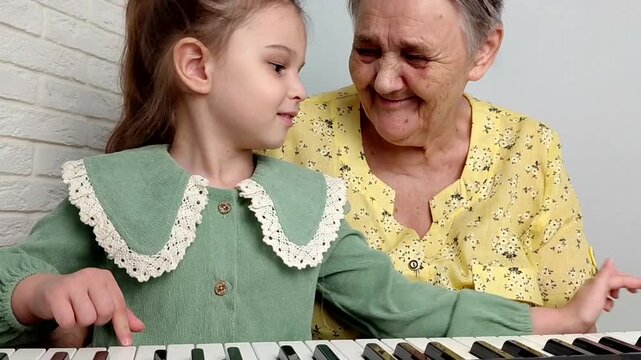 Elderly grandmother teaching little sweet girl playing piano, smiling with happiness, staying at cozy home, spending time together. Family, Love, Education Concept.
