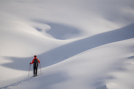 View of a solitary figure in a vibrant orange jacket traversing vast, pristine snow-covered slopes, creating crisp tracks in the white expanse, Bohinjsko jezero, Radovljica, Slovenia.