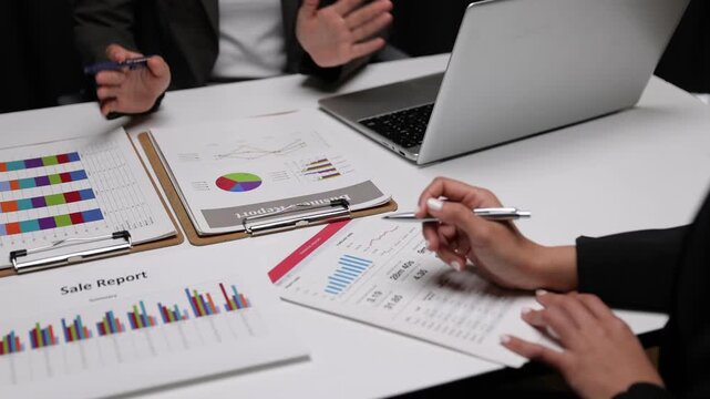 Businesswoman discussing financial charts during a late night meeting. Two dedicated female colleagues working overtime in office, analyzing financial data on documents and a laptop.