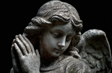 Obraz premium A serene angel statue with delicate features and folded hands, exuding tranquility against a dark background.