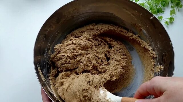 A person kneads the halva ingredients in a bowl with a spatula, preparing it. Various ingredients are visible in the finished mixture. Sunflower halva.