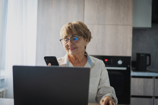 Smiling senior woman using laptop and smartphone at home for online banking or bill payment