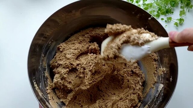 A person kneads the halva ingredients in a bowl with a spatula, preparing it. Various ingredients are visible in the finished mixture. Sunflower halva.
